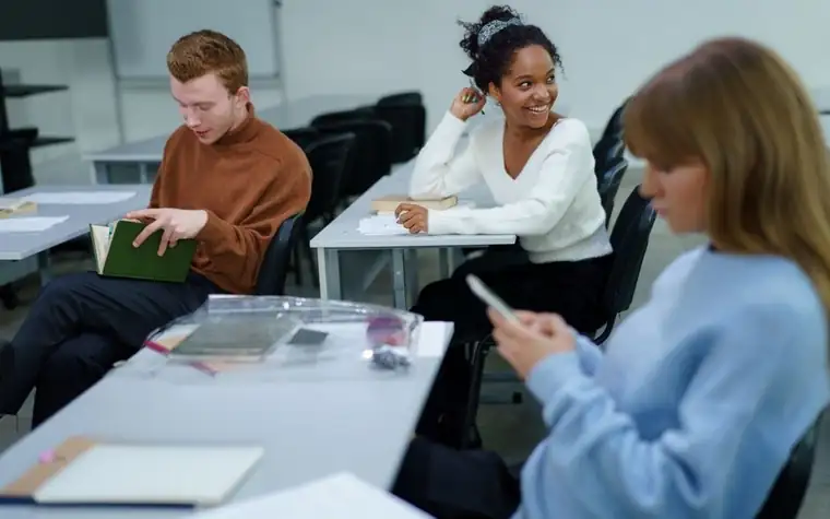 A student opening a book and looking at a smartphone screen