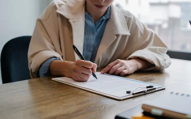 A woman sitting at a desk reviewing documents and writing something, filling out an application form