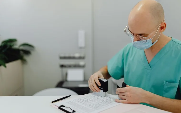 A medical worker in scrubs stamping a document