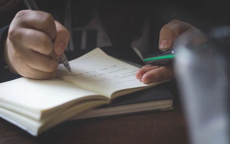 A hand writing in a notebook against a dark background