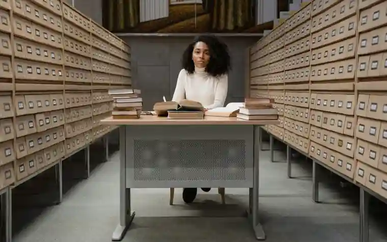 A learner at a desk between library shelves with an open book