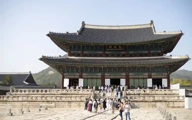 Visitors walking across the courtyard in front of a historic palace hall in the sunlight
