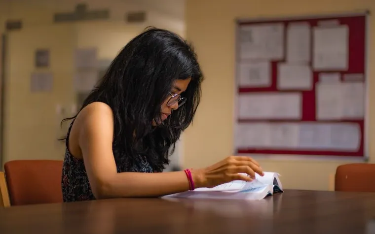 A woman studying with her notes at a reading table in a library
