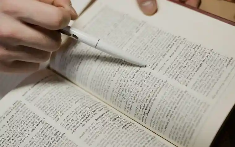 A hand using a pen tip to follow a line in an English dictionary