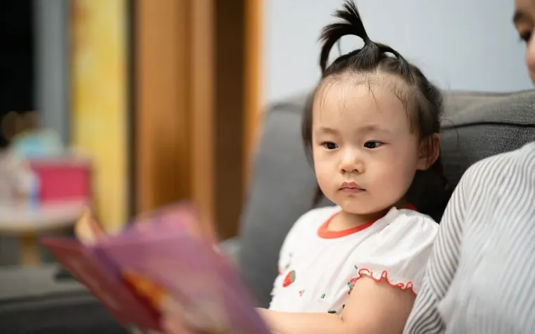 소파에 앉아 어른이 읽어 주는 이야기에 귀 기울이는 어린아이