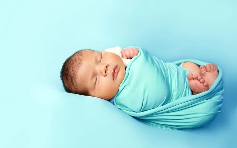 A newborn baby sleeping, swaddled in blue cloth