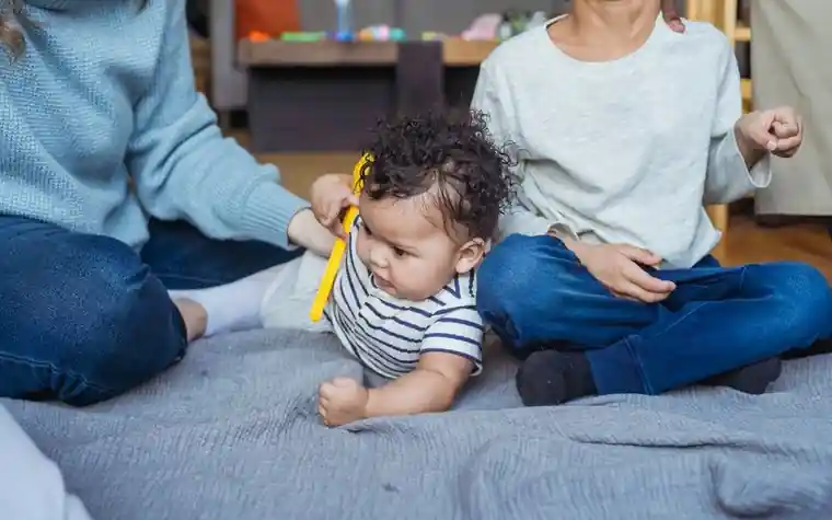 A baby lying on a floor mat next to parents who are sitting beside it