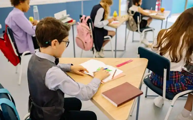 책상에 앉아 학습지를 푸는 초등학생과 지나가는 교사