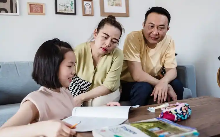 거실 소파에서 부모가 딸의 공부를 함께 살펴보는 모습