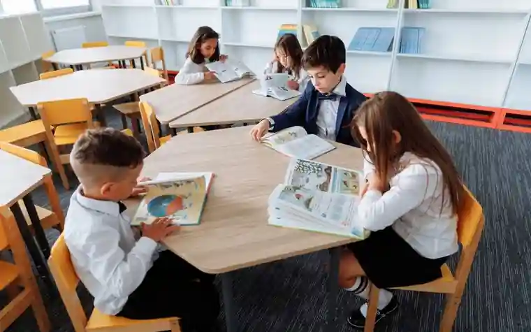 Elementary school students sitting around a library table reading books