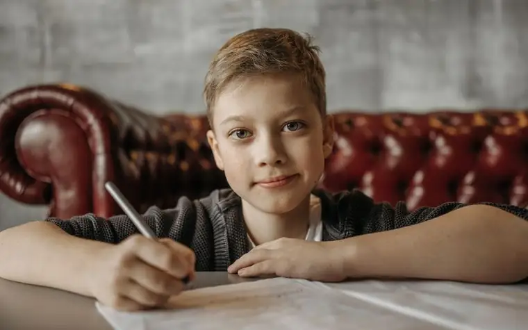 A boy sitting on a sofa writing on a sheet of paper