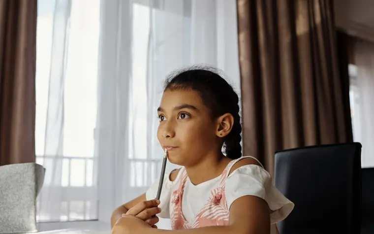 A girl sitting at a desk holding a pencil, lost in thought