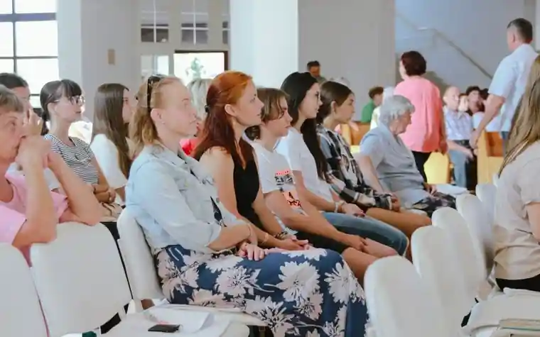 People sitting in rows in a hall-like room, listening to a briefing