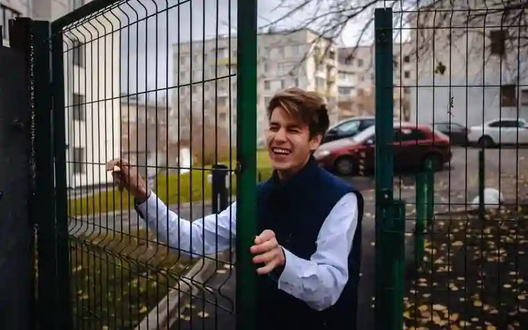A student laughing and opening the gate of a school metal fence among autumn leaves