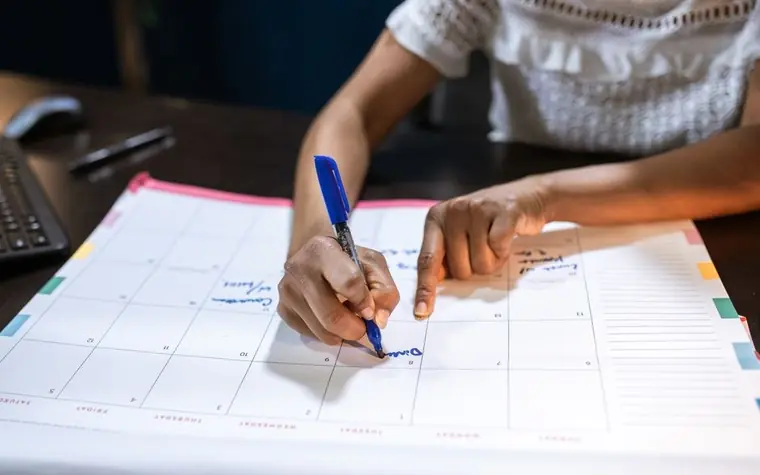 A hand marking a date on a desk calendar to check the schedule
