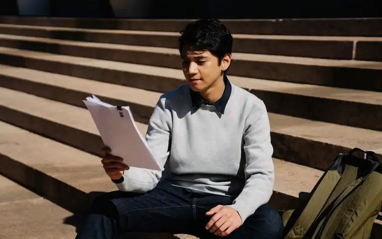 A student sitting on sunlit steps looking over documents