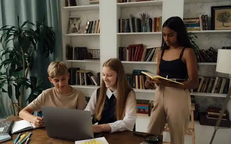 Teenagers sitting around a desk studying together with a laptop and books