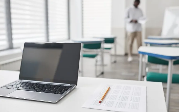 A laptop and an exam sheet lying on a desk in a classroom