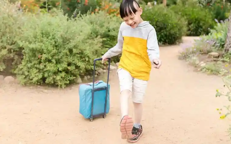 파란 여행용 캐리어를 끌며 웃고 걷는 어린아이