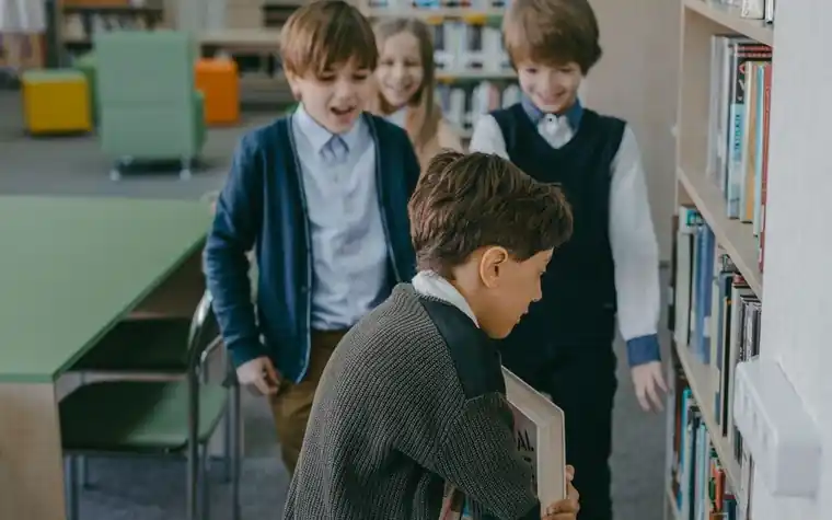 Elementary school children walking in a line along a corridor beside a library bookshelf