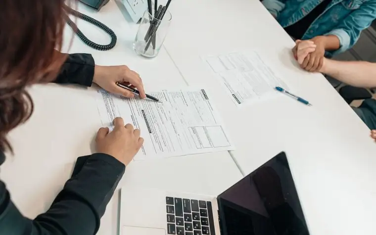A hand writing on an application form on a table with a pen