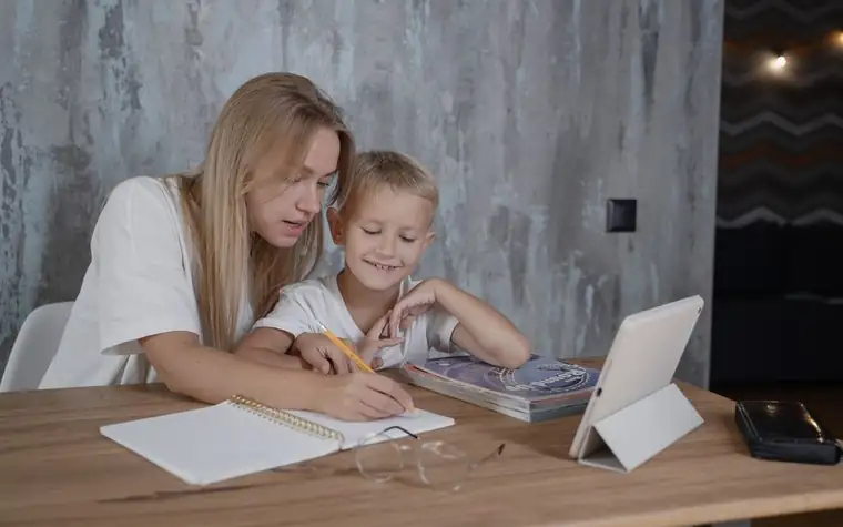 A mother and child sitting at a table and writing with a pencil while going over homework together