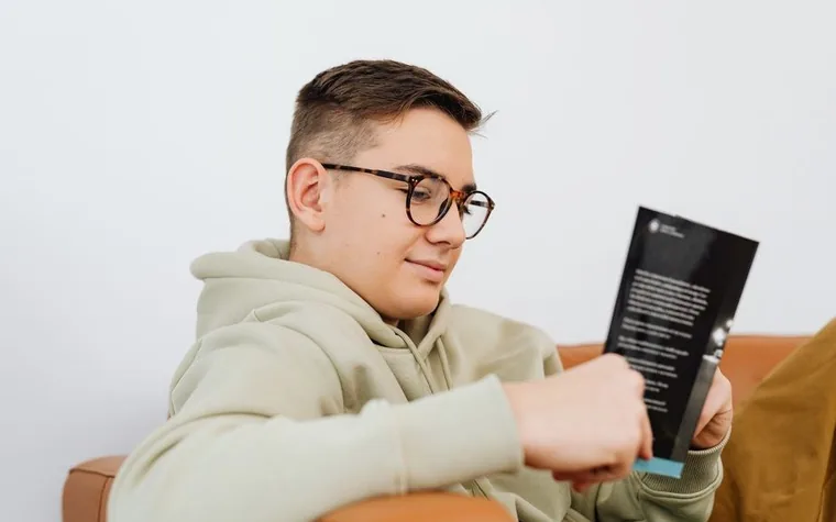 안경을 쓴 학생이 팜플렛을 읽고 있는 모습
