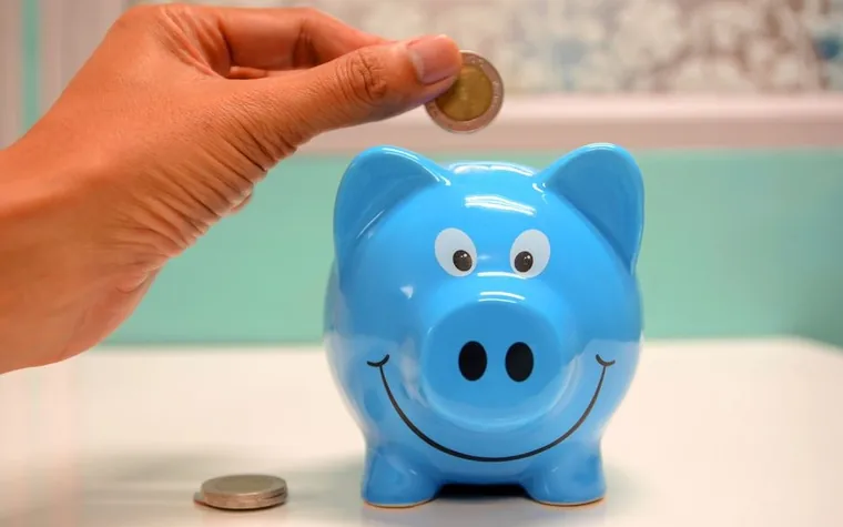 A hand putting a coin into a blue piggy bank