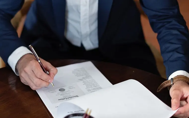 A person in a suit signing a document with a pen