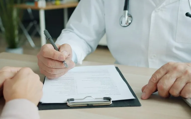 The hands of a doctor and a patient signing a medical form