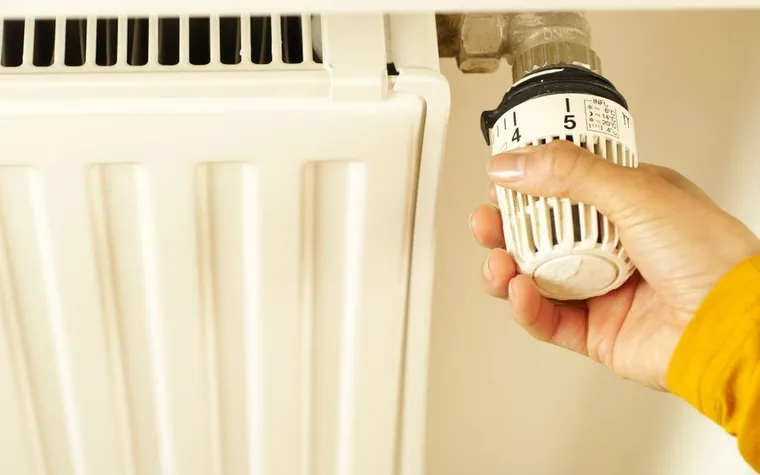 A hand turning the temperature control valve on a radiator