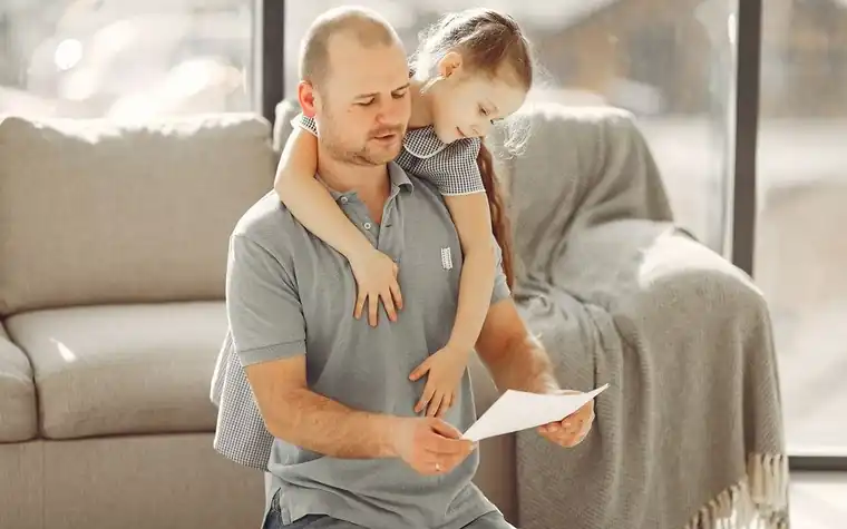A father holding his daughter on a sofa while reading a notice