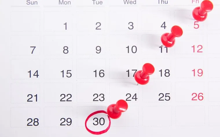 A wall calendar with red pins on several dates and the 30th circled