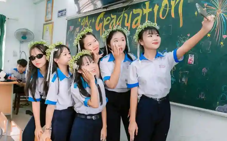 Students wearing flower crowns taking a group photo in front of a blackboard that reads Graduation