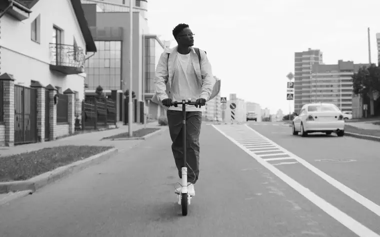 도시 도로의 차선 옆에서 전동킥보드를 타고 가는 사람